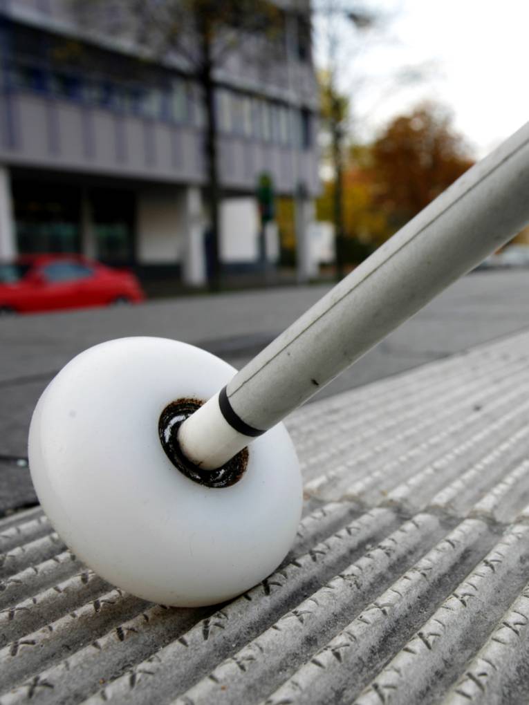 Ein weißer Langstock mit rollender Kugelspitze wird über ein Rillenplattensystem geführt.