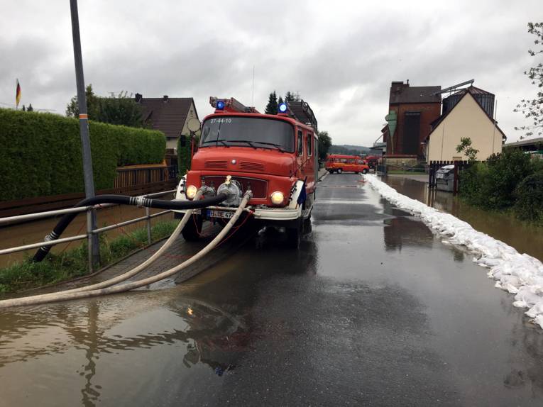 Ein Feuwerhrfahrzeug auf überfluteter Straße. Am Fahrzeug ist eine Vorbaupumpe montiert, die das Wasser abpumpt.