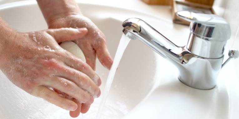 Eine Person seift sich mit einem Seifenstück neben fließendem Wasser die Hände ein.