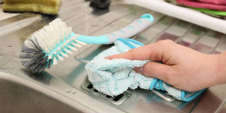 Hand mit Putzlappen an einem Edelstahlgeschirrspülbecken