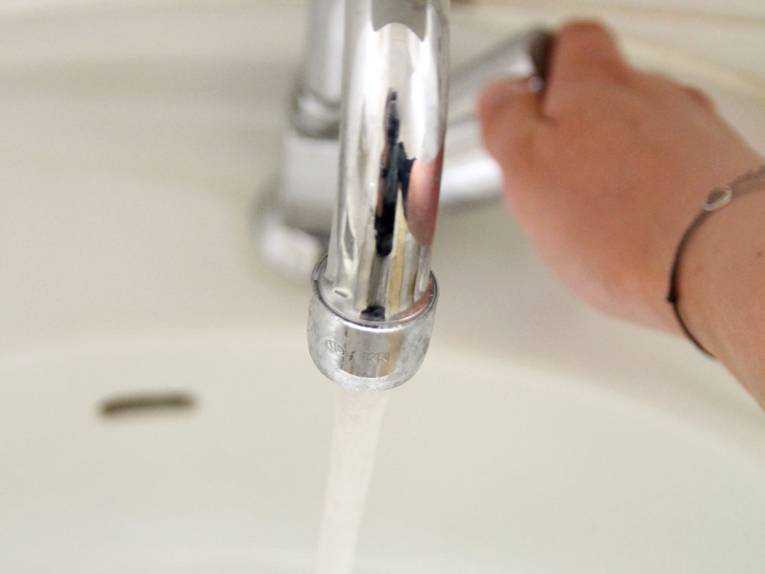 Zu sehen sind eine Hand und ein Waschbecken mit laufendem Wasserhahn.