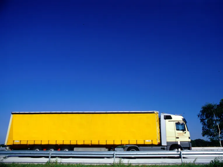 Ein gelber LKW auf einer Fahrbahn mit Leitplanken.