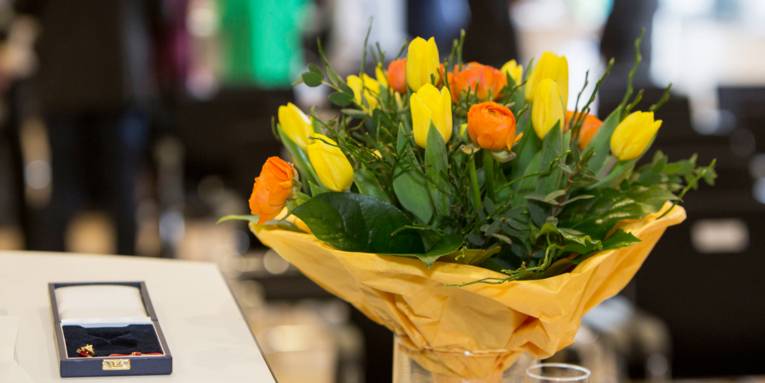 Neben einer Schachtel, in der ein Orden aufbewahrt werden kann, steht ein Blumenstrauß mit gelben und orangefarbenen Blüten.