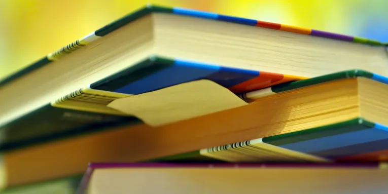 Blick von unten auf einen ungeordneten Stapel von Büchern. Sie scheinen im intensiven Gebraucht, wahrscheinlich zum Nachschlagen und Lernen. Es haftet ein Klebezettel unter einen Buch.