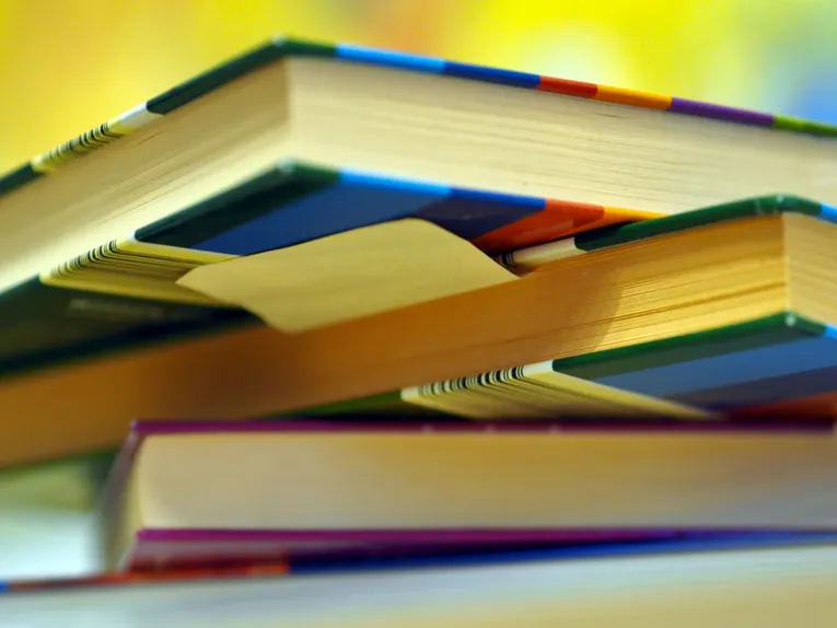 Blick von unten auf einen ungeordneten Stapel von Büchern. Sie scheinen im intensiven Gebraucht, wahrscheinlich zum Nachschlagen und Lernen. Es haftet ein Klebezettel unter einen Buch.
