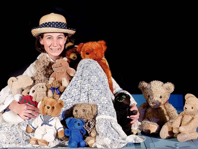 Frau mit Hut zwischn zahlreichen Teddybären. 