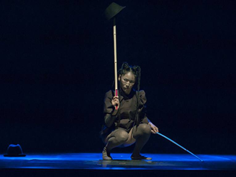 Die Tänzerin Minako Seki in der Hocke mit zwei Bambusstäben