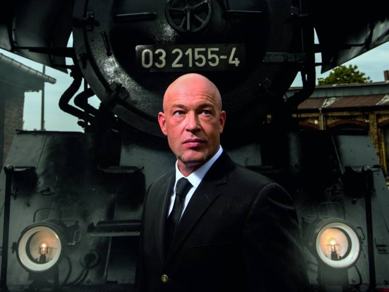 Ein Mann mit Glatze vor einer Dampflok.