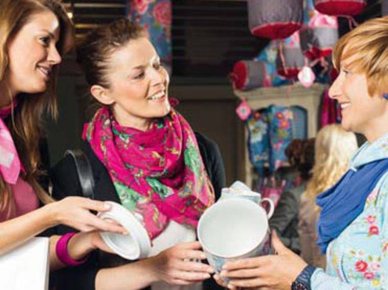 Drei junge Frauen unterhalten sich angeregt und halten dabei Dekorationsartikel in den Händen.