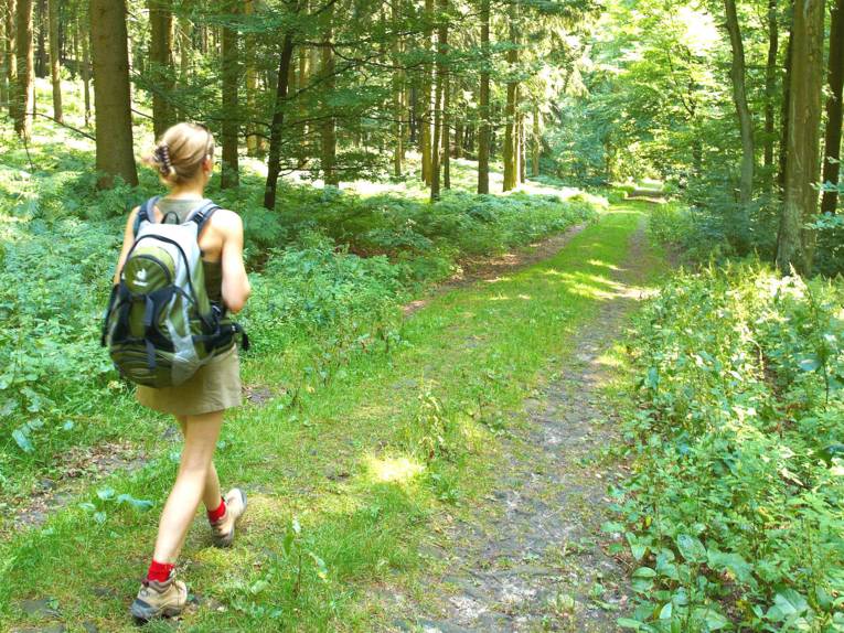 Eine Frau mit Rucksack wandert auf einem Waldweg. 
