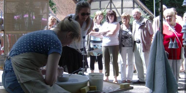 Besucher sehen einer Frau beim handwerken zu.