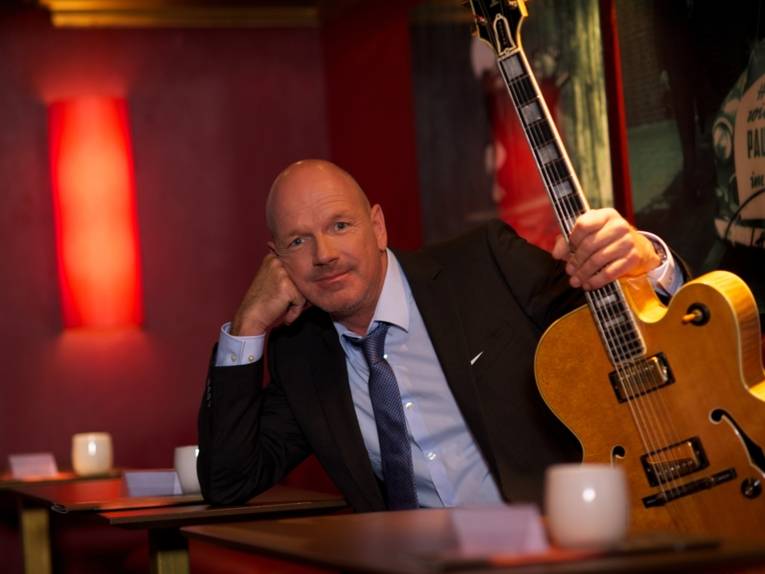 Knut Richter sitzt lässig an einem Tisch mit der Gitarre in der Hand.