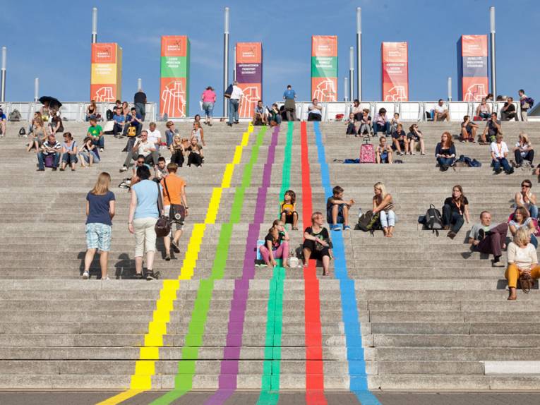 Menschen sitzen auf einer Treppe mit farbigen Linien.