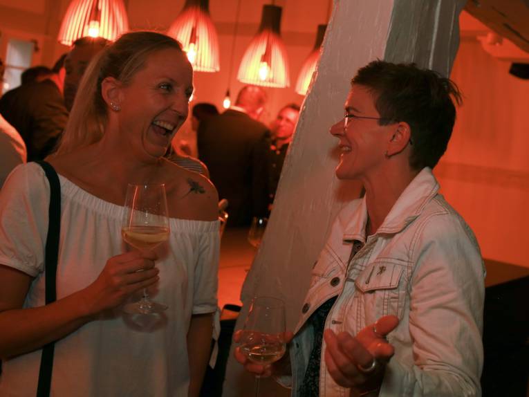 Zwei Frauen mit einem Glas in der Hand unterhalten sich.