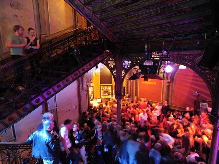 Menschen in einem farbig ausgeleuchtetem, breiten Treppenhaus