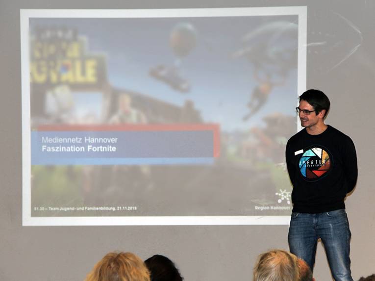 Ein Mann steht vor einer Leinwand vor Publikum und scheint einen Vortrag zu halten.