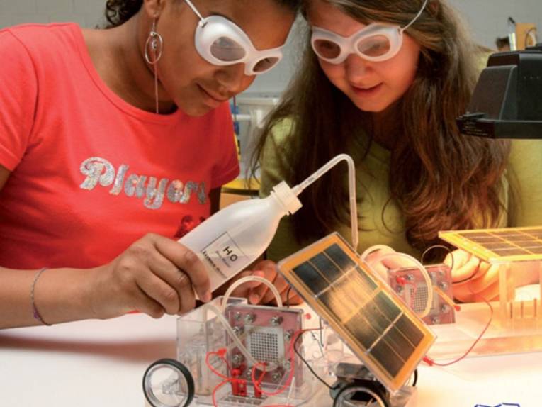 Zwei Schülerinnen mit Schutzbrillen arbeiten mit einem kleinem Solarmobil