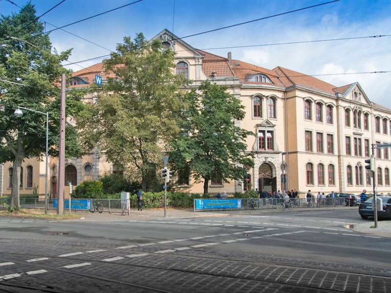 Die Schule Auf dem Loh ist ein dreistöckiges historisches Gebäude mit hohen Räumen und Ziegeldach in der Nähe einer Straßenkreuzung, die mit einem Gitter gesichert ist