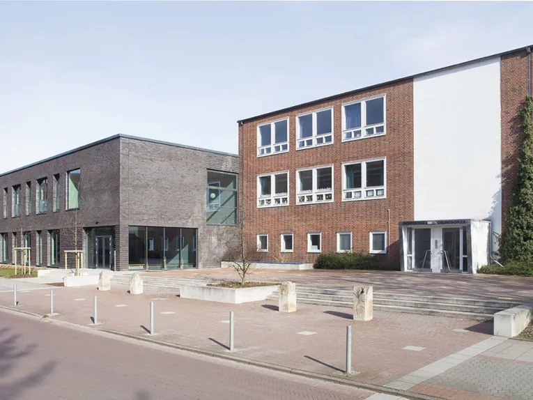 Grundschule Fichteschule: ein dreistöckiges Backsteingebäude, das von der Straße zurückgesetzt ist. Daneben der zweigeschossige Mensaanbau in dunklerem Backstein.