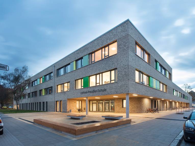 Außenaufnahme der Otfried-Preußler-Schule: ein modernes dreistöckiges Gebäude aus hellem Klinker, bei dem der Eingangsbereich etwas zurückgesetzt ist