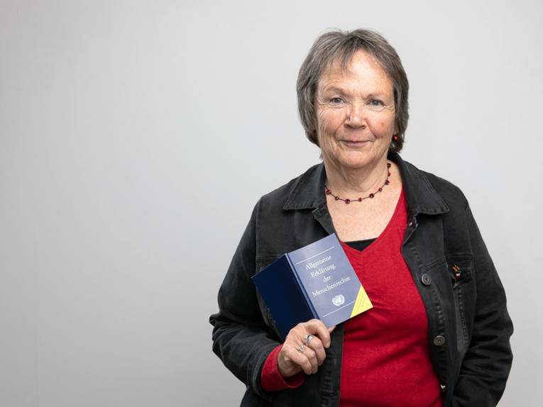 Eine Frau lächelt und hält ein Buch mit dem Titel "Allgemeine Eklärung der Menschenrechte" in die Kamera.