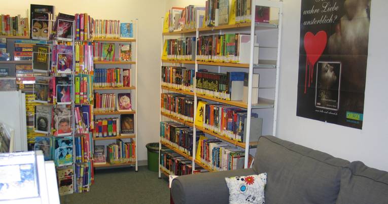 graues Sofa, Taschenbuchständer, Filmplakate im Jugendbereich