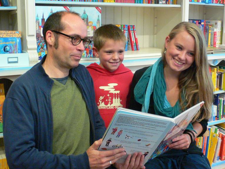 Ein Mann, ein Junge und eine Frau halten ihr Buch lächelnd in die Kamera.