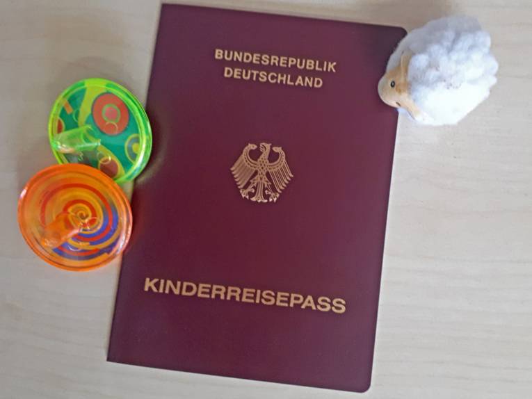 Neben einem Dokument mit rotem Einband und der Aufschrift Kinderreisepass liegt Kinderspielzeug.