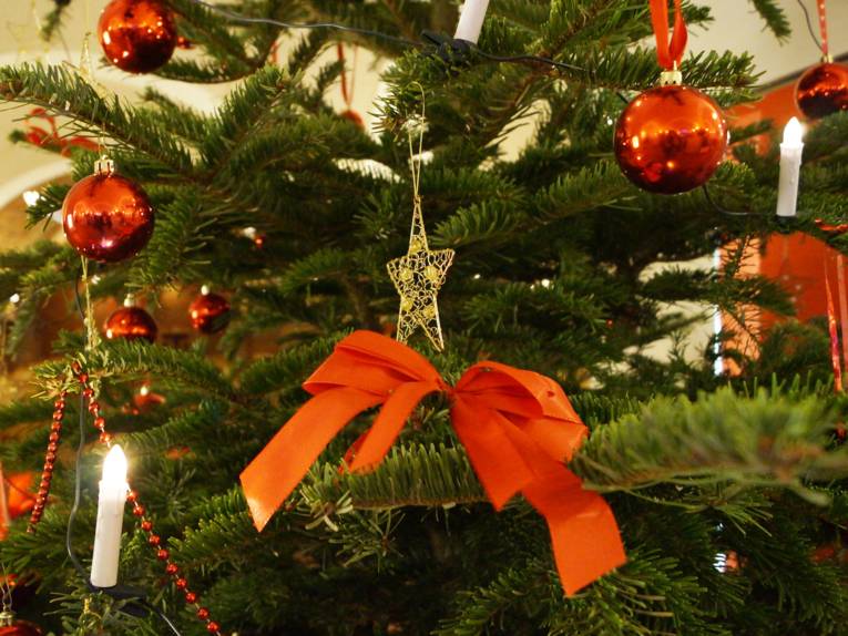 Ein traditionell geschmückter Weihnachtsbaum mit roten Kugeln, goldenen Sternen und elektrischen Kerzen