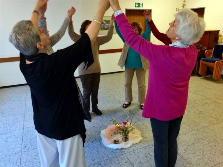 Mehrere Senioren stehen im Kreis um eine Kerze und halten sich die Hände und strecken dabei die Arme nach oben.