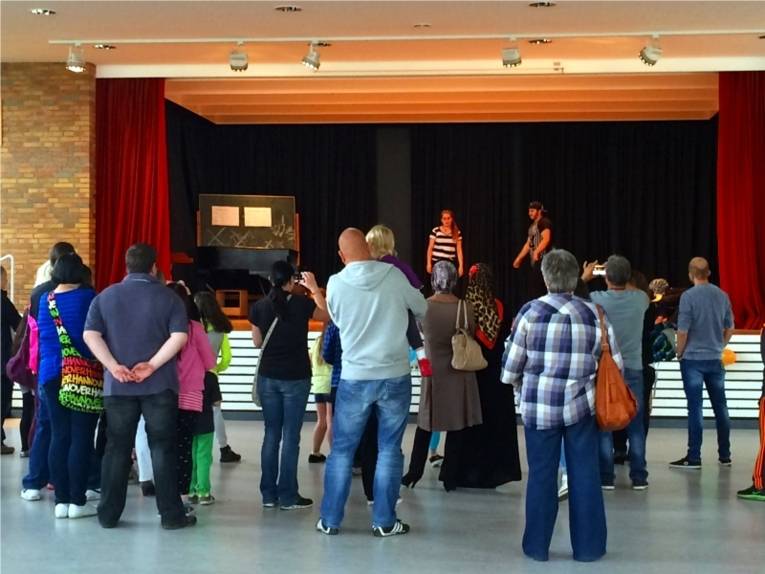 Die Besucherinnen und Besucher schauen sich die Hip Hop AG der Heisterbergschule an. Die Aufführung wurde in einem größeren Saal auf einer Bühne aufgeführt.