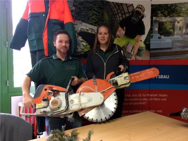 Ein junger Mann und eine junge Frau stehen an einem Informationstand und präsentieren Geräte, die sie im Fachbereich Umwelt und Stadtgrün in ihrer Ausbildung verwenden.