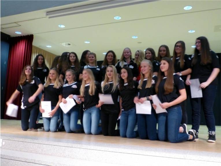 Viele junge Frauen stehen und knien auf der Bühne. Dabei haben sie eine Urkunde in der Hand. 