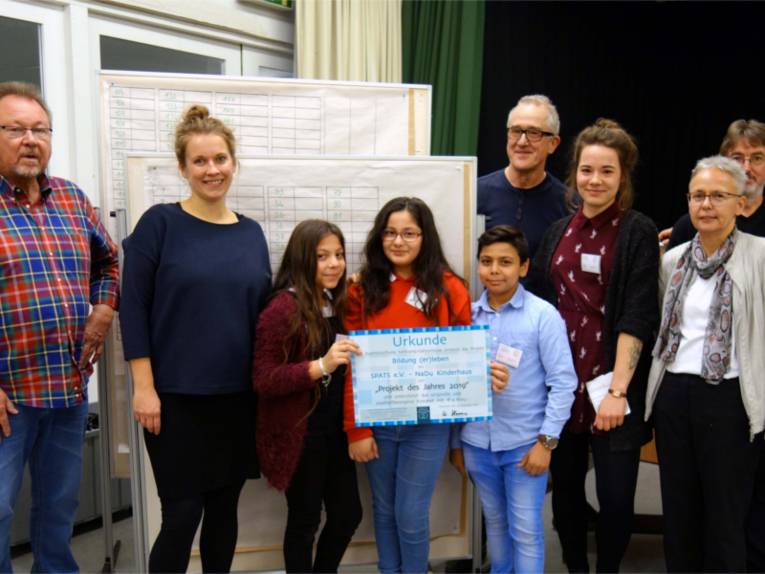 Auf dem Bild sind Erwachsene und Kinder zu sehen. Die Kinder halten eine Urkunde in der Hand.