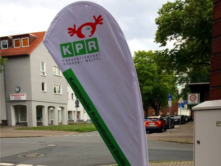 Auf dem Bild ist eine Werbefahne des KPR-Döhren-Wülfel zu sehen. Im Hintergrund sind Häuser, Autos und Bäume zu sehen.