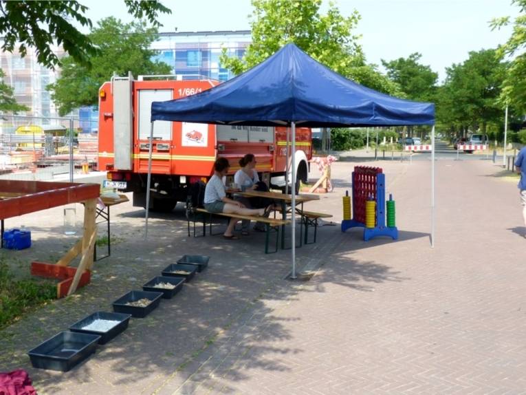 Auf dem Bild ist ein älteres Feuerwehrauto namens JuKiMob zu sehen. Daneben ist ein Pavillon aufgestellt mit Spiel-Aktionen für Kinder. 