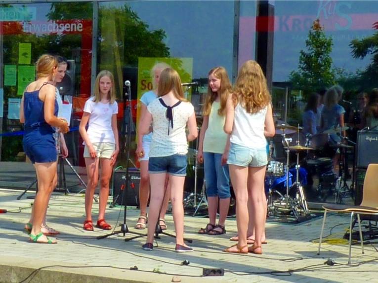 Sieben junge Frauen stehen im Kreis auf der Bühne und singen gemeinsam.