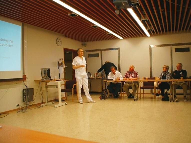 Ein deutscher Arzt steht in einem Raum vor mehreren BesucherInnen und Besuchern und diskutiert mit ihnen zusammen zu aktuellen Themen in der Medizin.