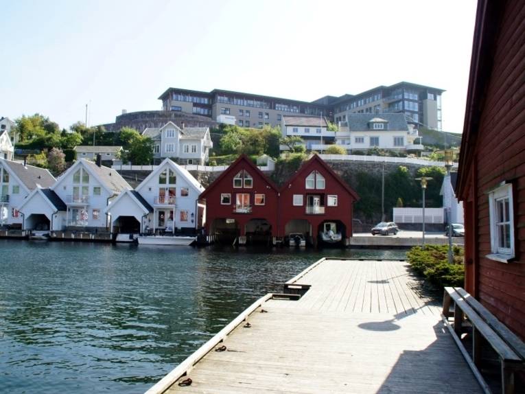 Das Krankenhaus in Flekkefjord von außen. Das Krankenhaus steht auf einem Berg. Darunter stehen gepflegte Häuser an einem Gewässer.