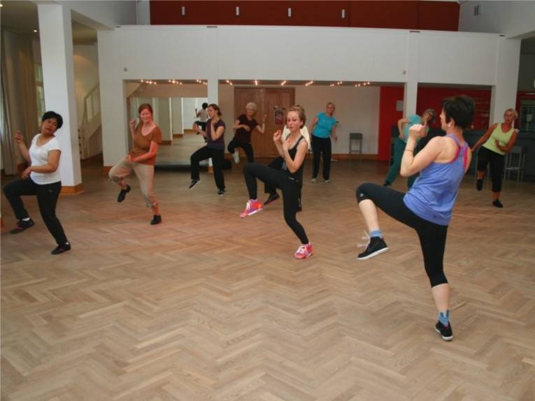 Eine Tanzlehrerin tanzt vor einer Gruppe von Frauen einen Tanz vor, und die Frauen tanzen nach.