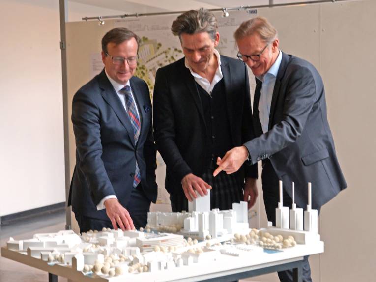 Drei Männer, die auf ein Architekturmodell zeigen. 
