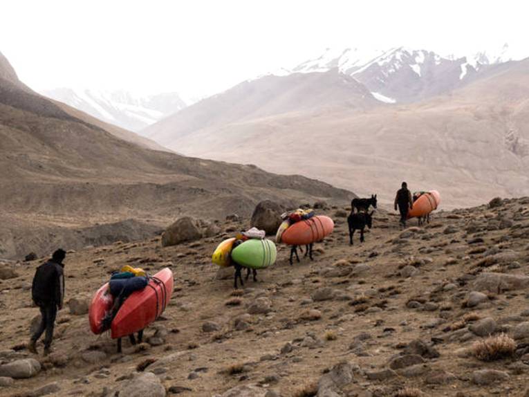 Die bergige Landschaft von Tadschikistan. Kajaks werden auf Eseln über einen schmalen Pfad transportiert.