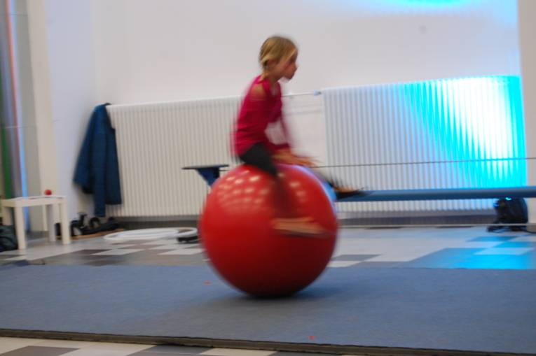 Ein Mädchen springt über eine große rote Kugel.