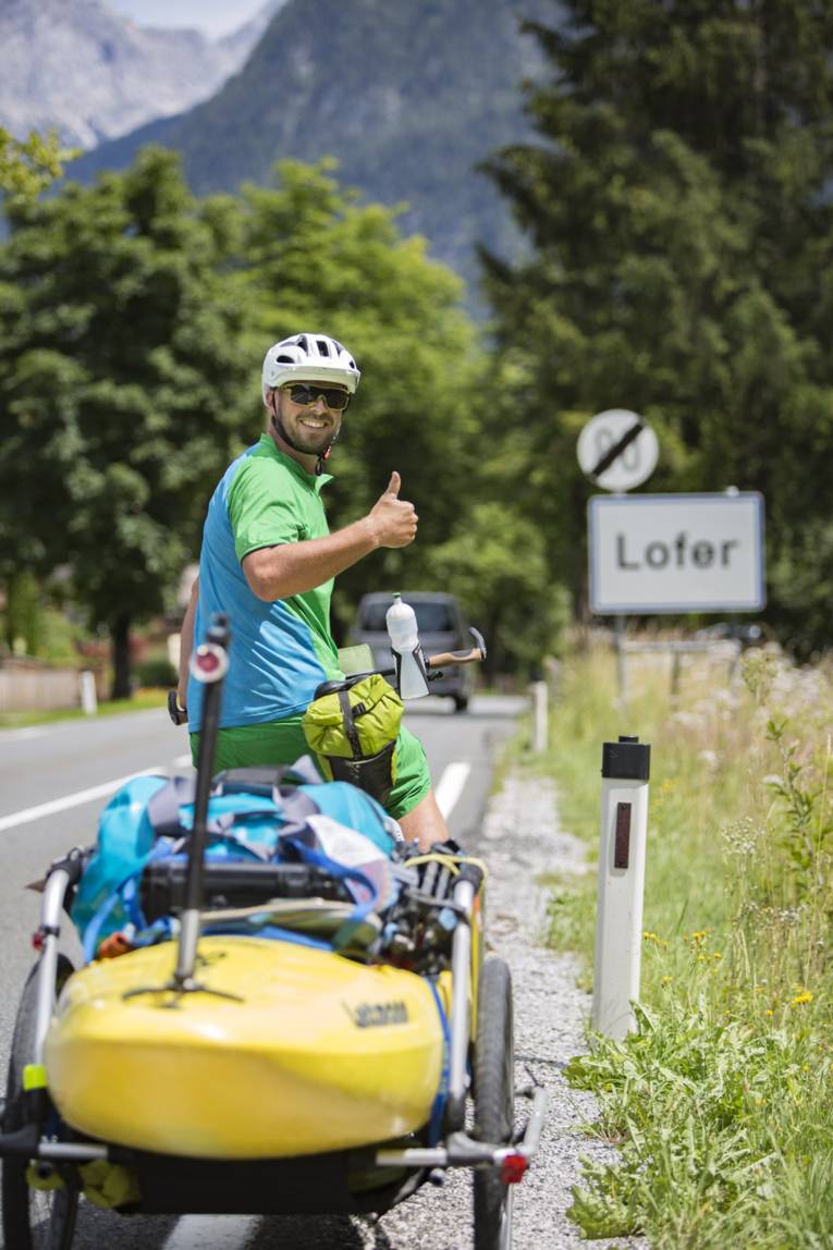 Ein Radfahrer steht vor einem Straßenschild und hebt den Daumen.