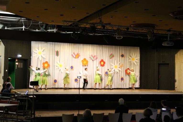 Die Tänzerinnen und Tänzer der Tanzgruppe Legende führen auf der Bühnen einen Tanz vor. Im Hintergrund hängen große Blüten an der Wand.