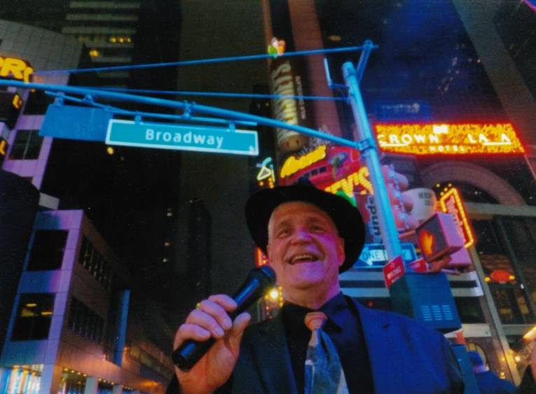 Ein Mann steht in New York unter dem Strassenschild vom Broadway.
