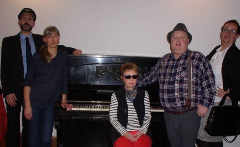 Fünf Personen stehen vor einem alten Klavier.