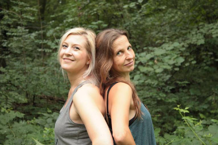 Zwei Frauen in Yoga-Kleidung stehen Rücken an Rücken.