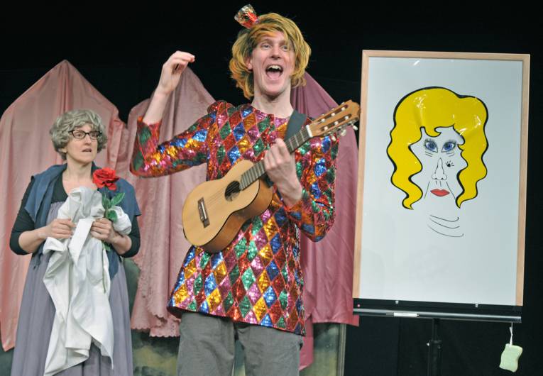 im Vordergrund singende, Ukulele spielende Person, zur Linken ältere Frau, zur Rechten gemaltes Bild von einem Gesicht