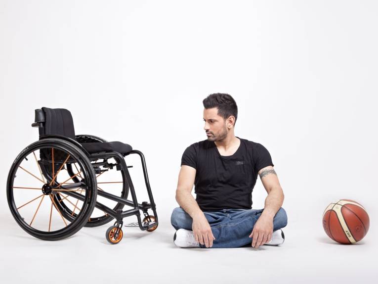 Zu sehen ist Tan Caglar mit seinem Rollstuhl und einem Basketball